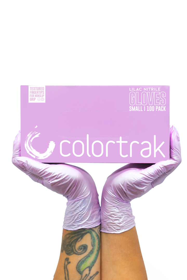 Two gloved hands holding a lilac box of Colortrak Lilac Frost nitrile gloves, 100 pack