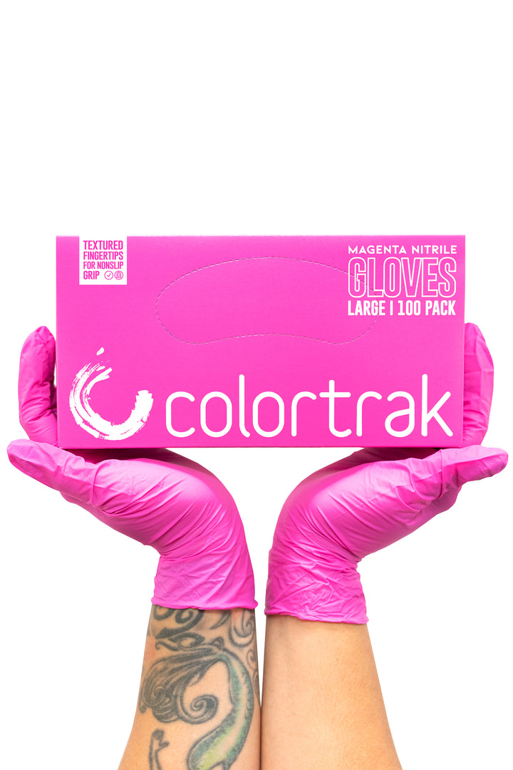 Two gloved hands holding a pink box of Colortrak magenta nitrile gloves, 100 pack