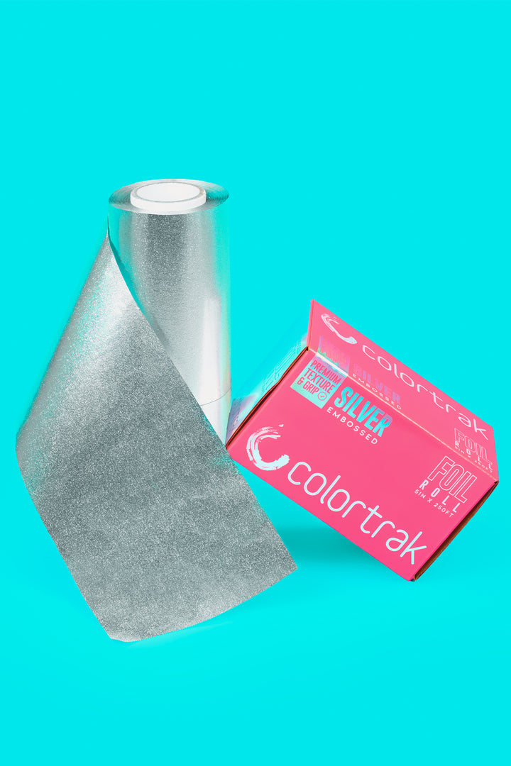 Embossed silver foil unrolling from the roll beside the pink box, on a teal background