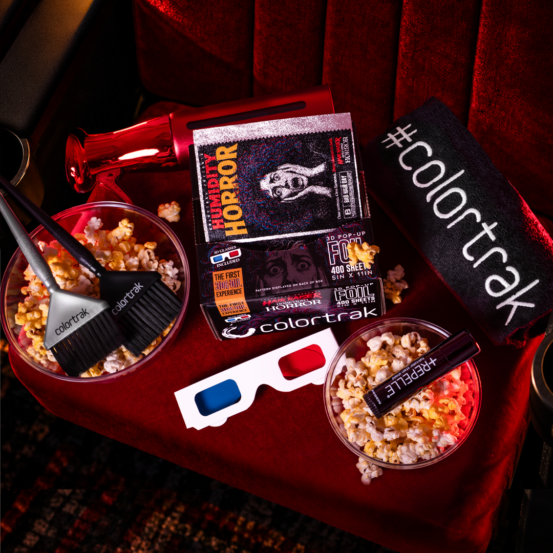 Hair Raiser 3D pop-up foil box on a red velvet movie theater seat with complementary Colortrak products: two color application brushes (Twin Touch Color Brushes), a red metallic spray bottle, a black #colortrak towel, and Repelle haircolor stain shield. Styled with 3D glasses and bowls of popcorn.