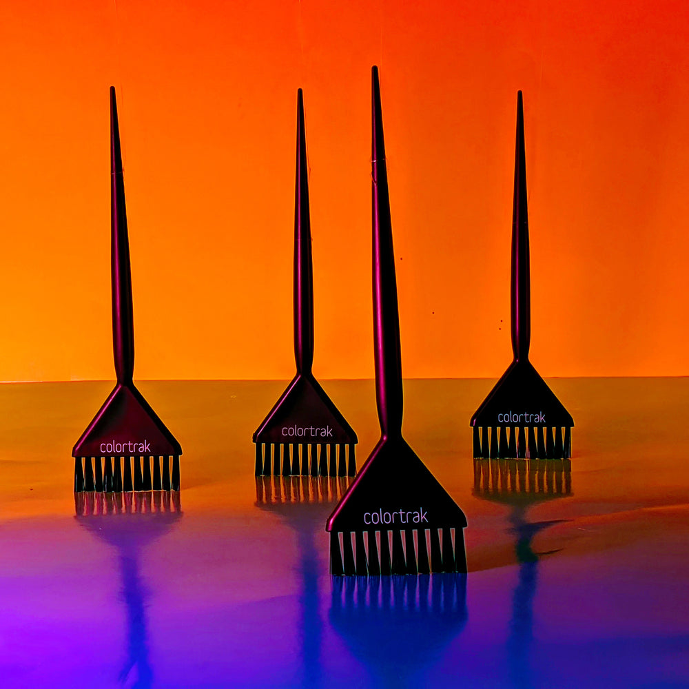 Four brushes standing upright on a glossy surface against an orange-to-purple background